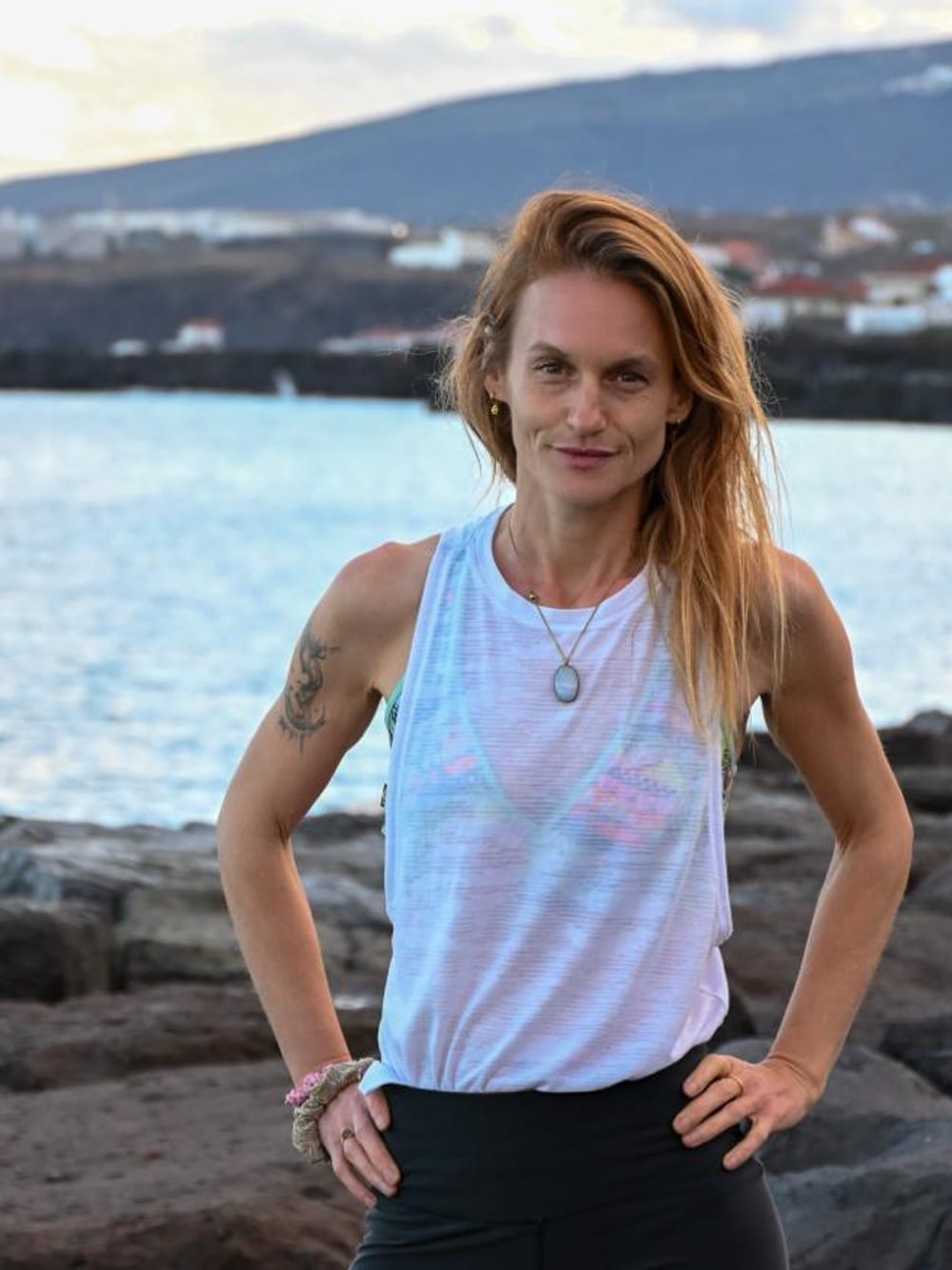 Ursula on the volcanic coast of Tenerife at sunset, the bay and mountains behind her.